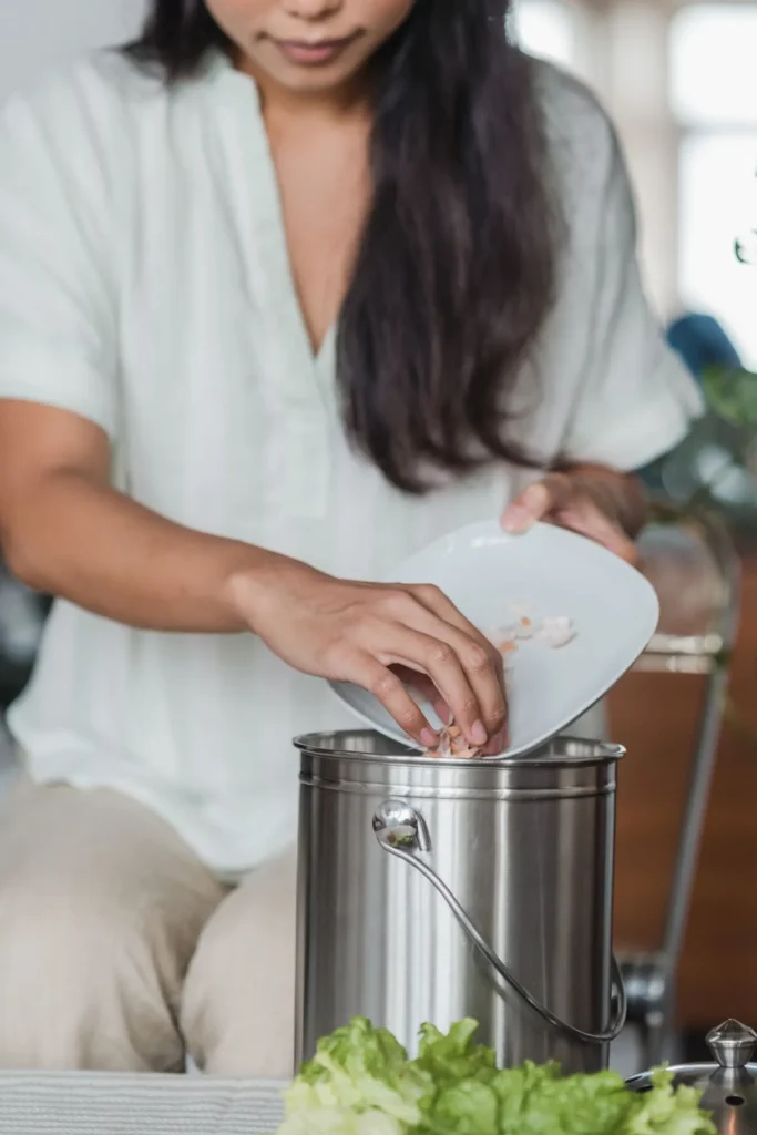 Une personne qui verse des épluchures dans un seau à compost en inox, dans une cuisine